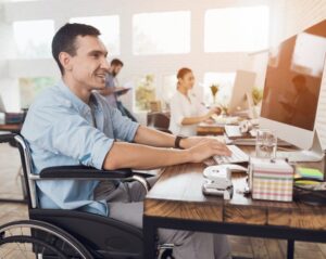 Man in a wheelchair working at a modern office desk with colleagues in the background