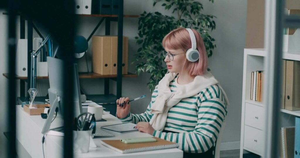 Young woman with pink hair and headphones working at a desk in a modern, accessible office