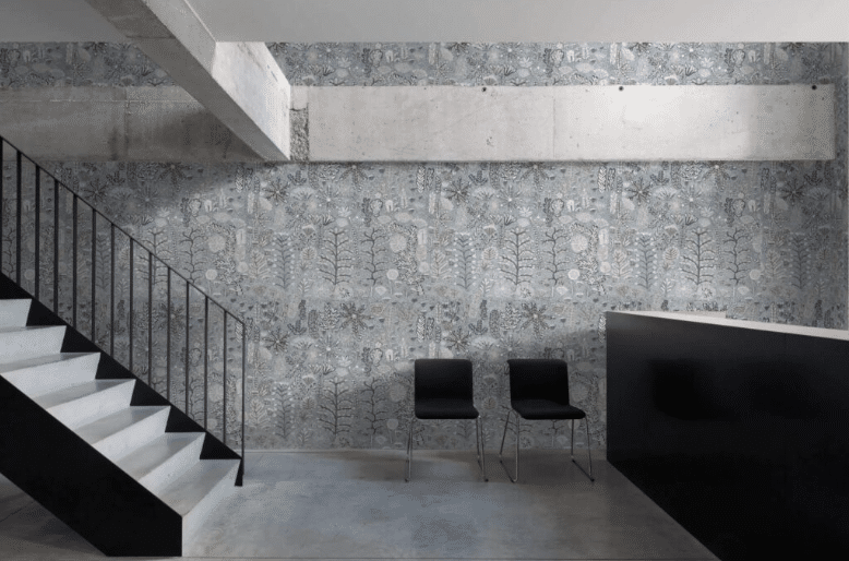 Industrial-style lobby with a patterned wallpaper, concrete features, and two black chairs beside a staircase.