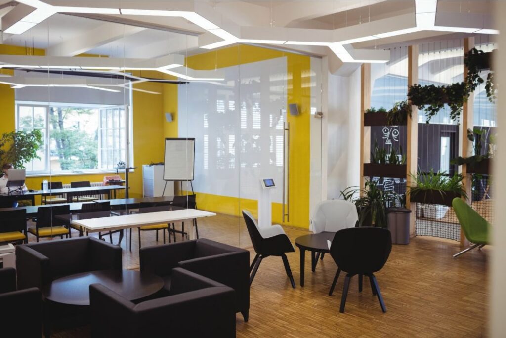 A modern, colourful office interior featuring a yellow accent wall, glass partitions, and a mix of casual lounge seating and formal workstations, representing a completed commercial office fitout timeline project.