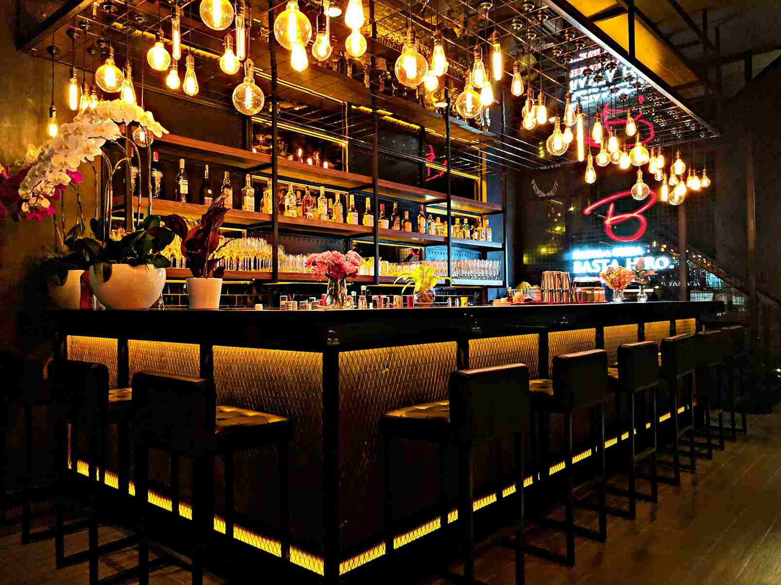 Modern hospitality bar fitout featuring warm pendant lighting, a black bar counter, upholstered seating and decorative shelving.