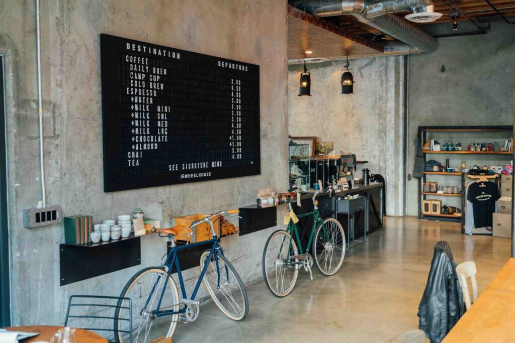 Industrial-style café fitout featuring polished concrete flooring, exposed ductwork, a black coffee menu board and timber furnishings.